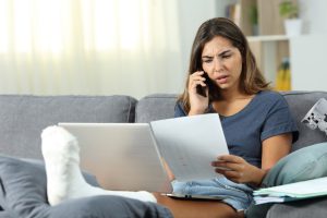 woman in a leg cast reads a bill while on the phone